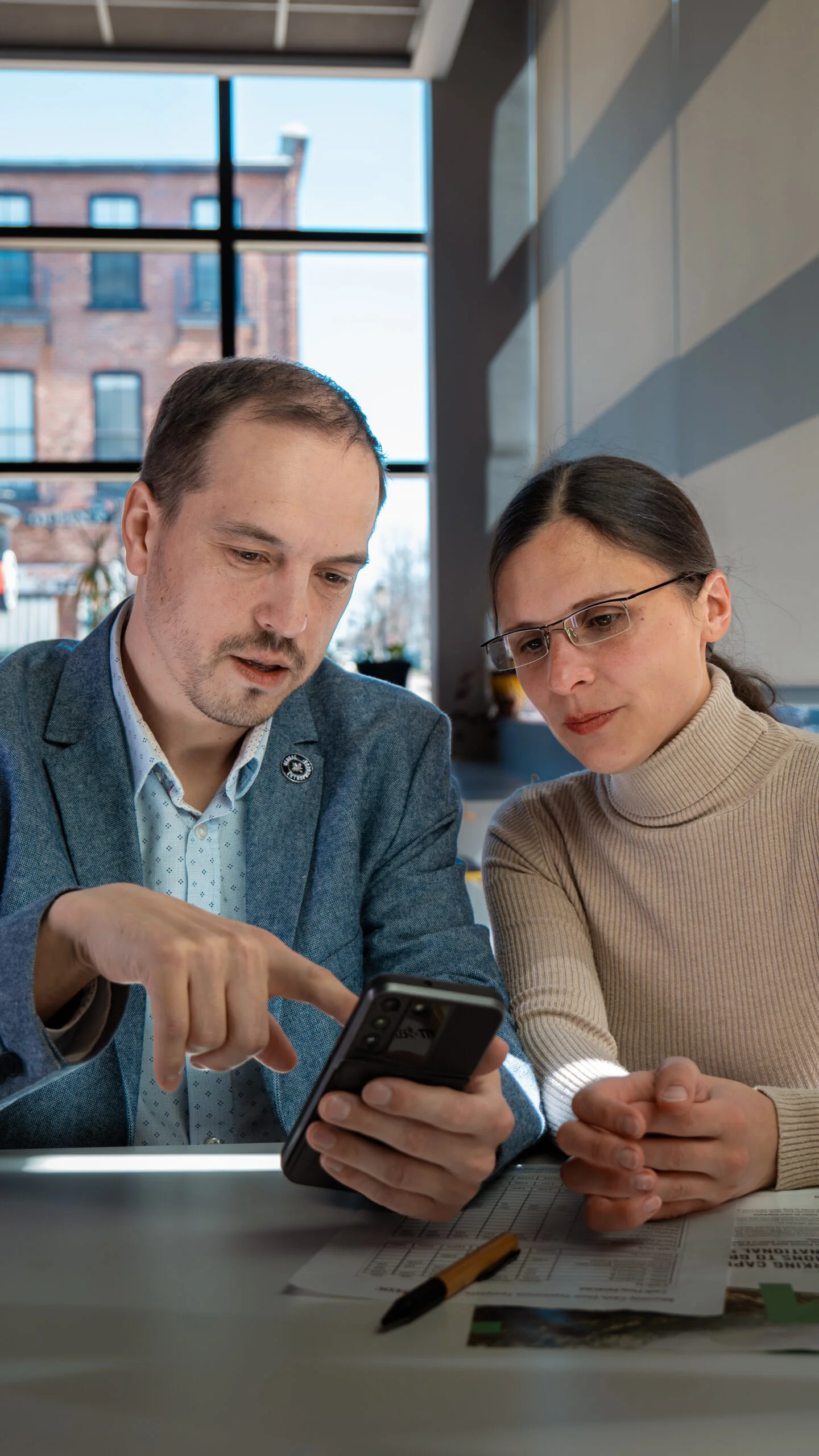 alex holding a phone while in discussion with another person as both stare at the phone.