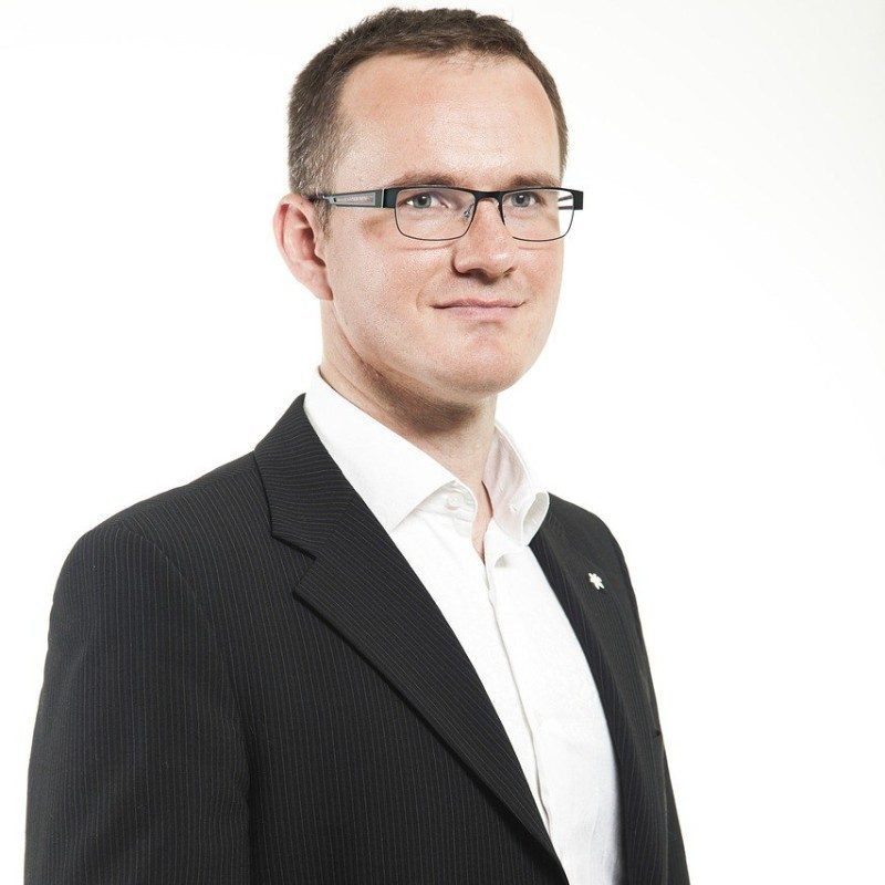 James Howell the development specialist wearing glasses and a black suit while staring at the camera